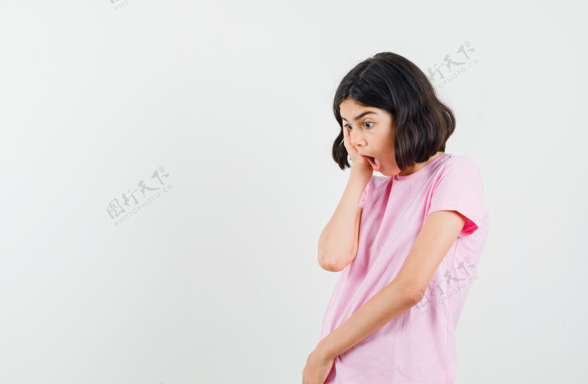 青少年小女孩手放在脸颊上 穿着粉色t恤 看起来很惊讶前视图青年看青少年