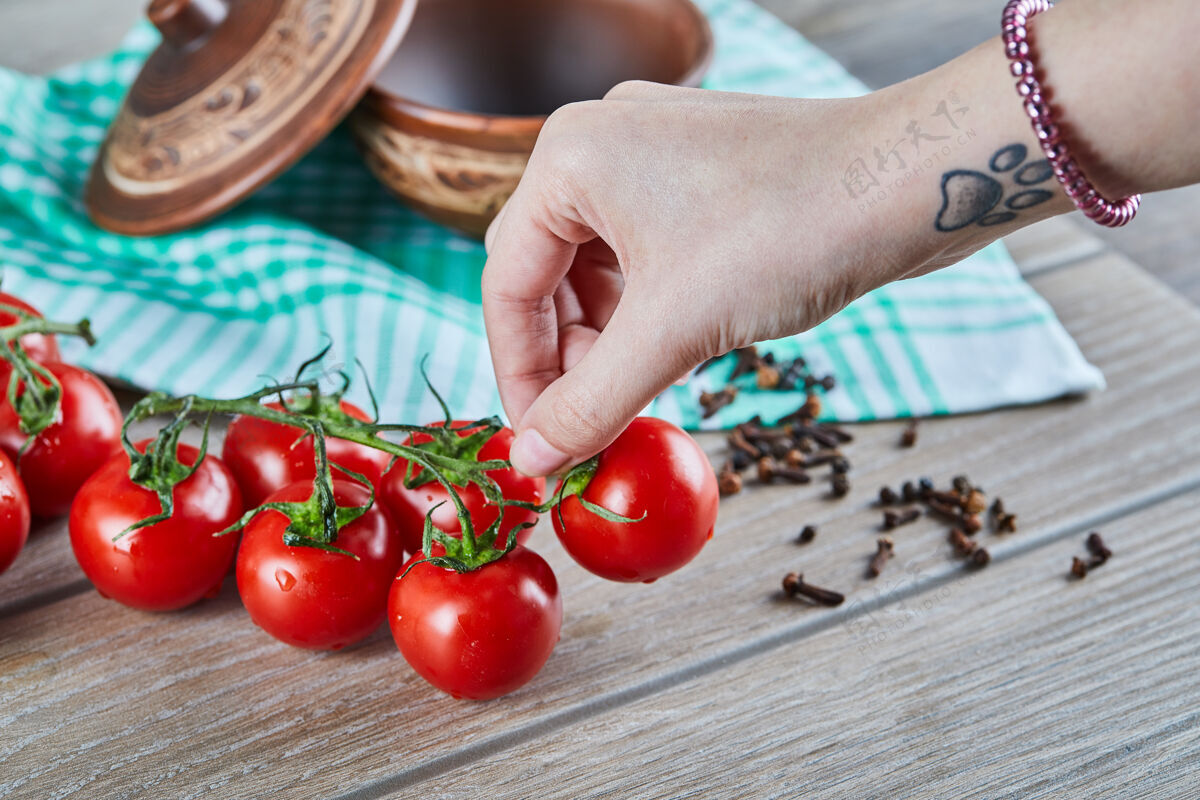 生的一堆西红柿和一个女人拿着一个西红柿放在木桌上素食团体滴