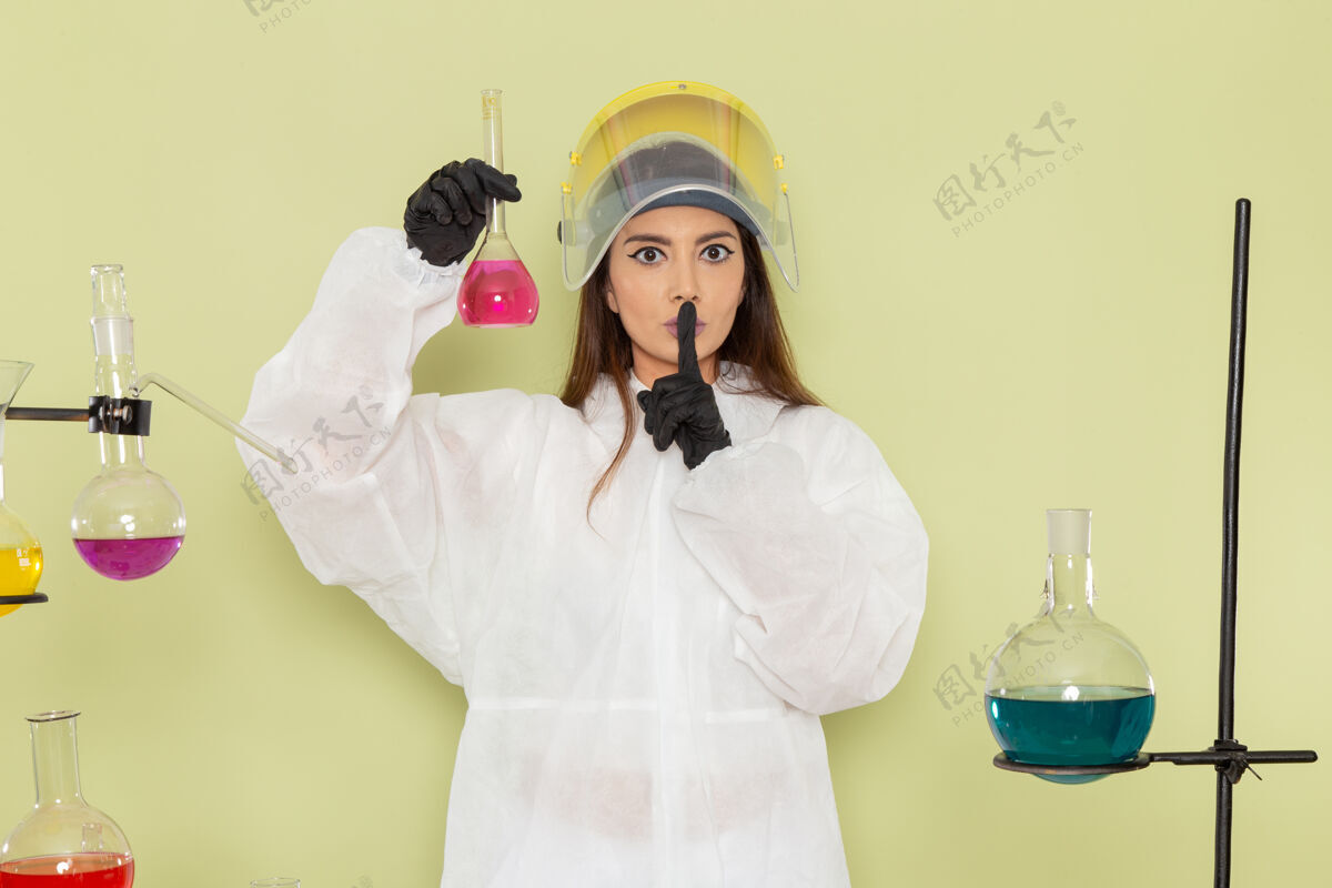 正面正面图身着特殊防护服的年轻女化学家在绿墙化学品上工作化学工作女科学实验室女性防护浴袍