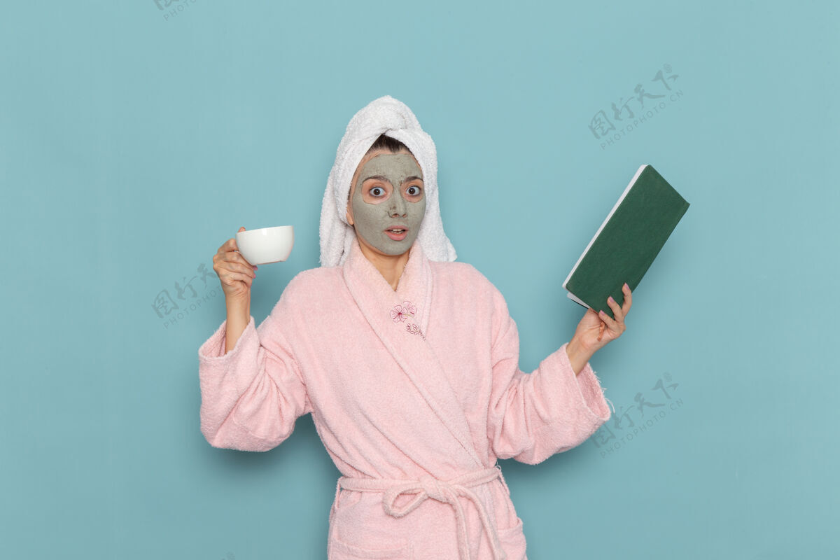 前正面图身着粉色浴袍的年轻女性淋浴后在蓝色墙壁上喝咖啡清洁美容净水自护霜淋浴自理浴袍抹刀