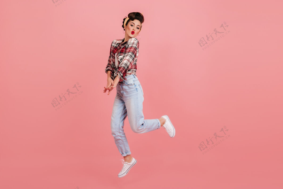 舞蹈无忧无虑的小女孩在粉色背景上跳跃一个穿着牛仔裤和格子衬衫的可爱年轻女子的摄影棚镜头人物牛仔裤粉色背景