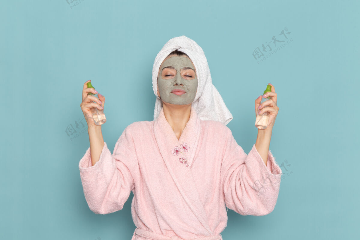 化妆品正面图年轻女性穿着粉色浴袍淋浴后拿着卸妆液在蓝色墙壁上美容水霜自护淋浴人男人举行