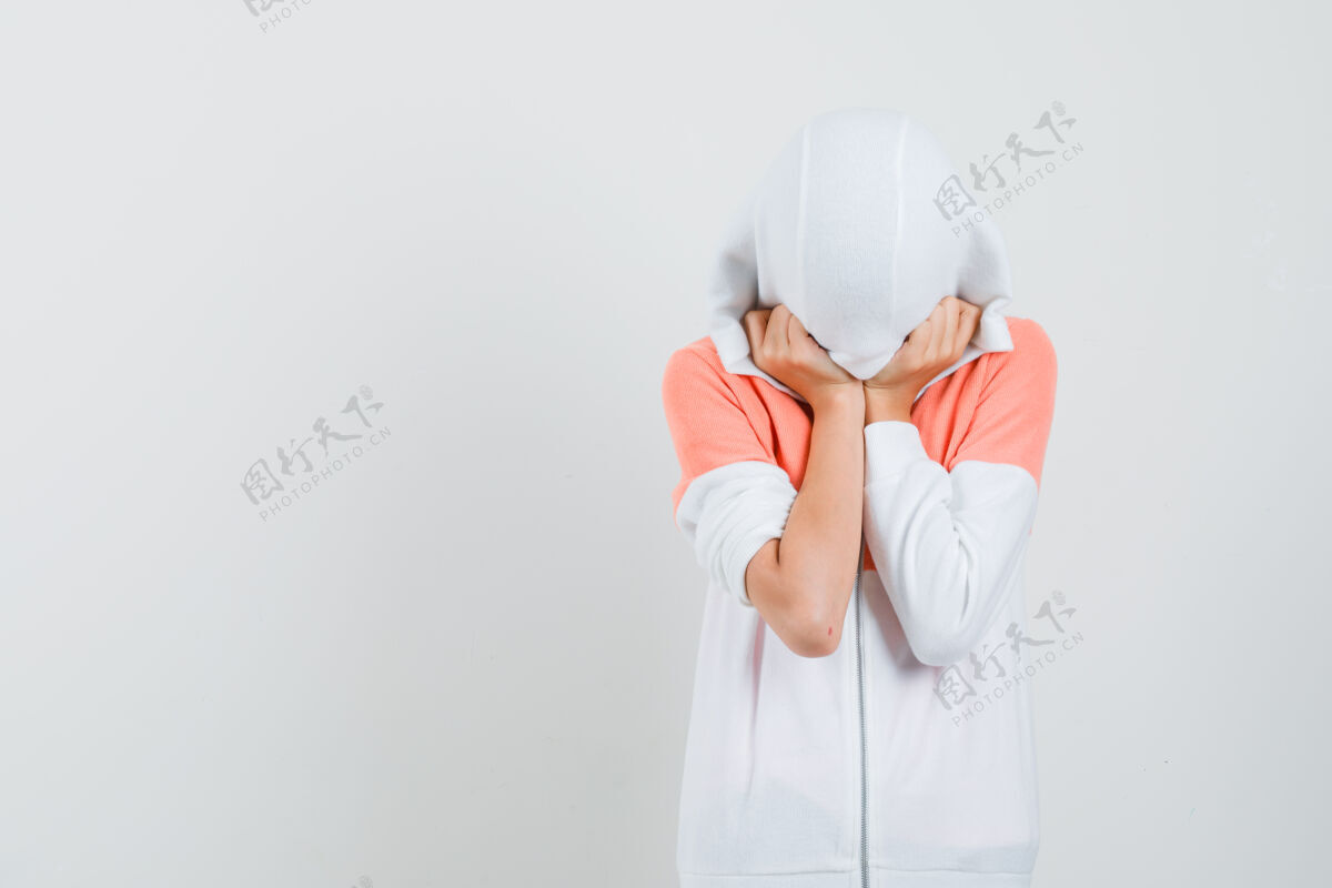 表情十几岁的女孩戴着白色夹克的帽子遮住她的头和脸 看起来很隐蔽时尚女人女性