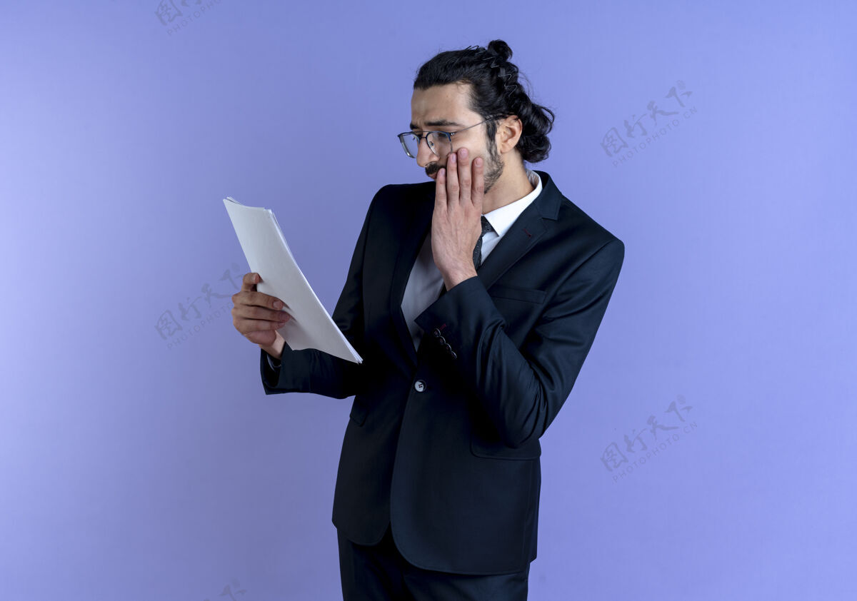 家伙一个穿着黑西装戴着眼镜的商人站在蓝色的墙上 用手捂着脸看文件生意生意人公司