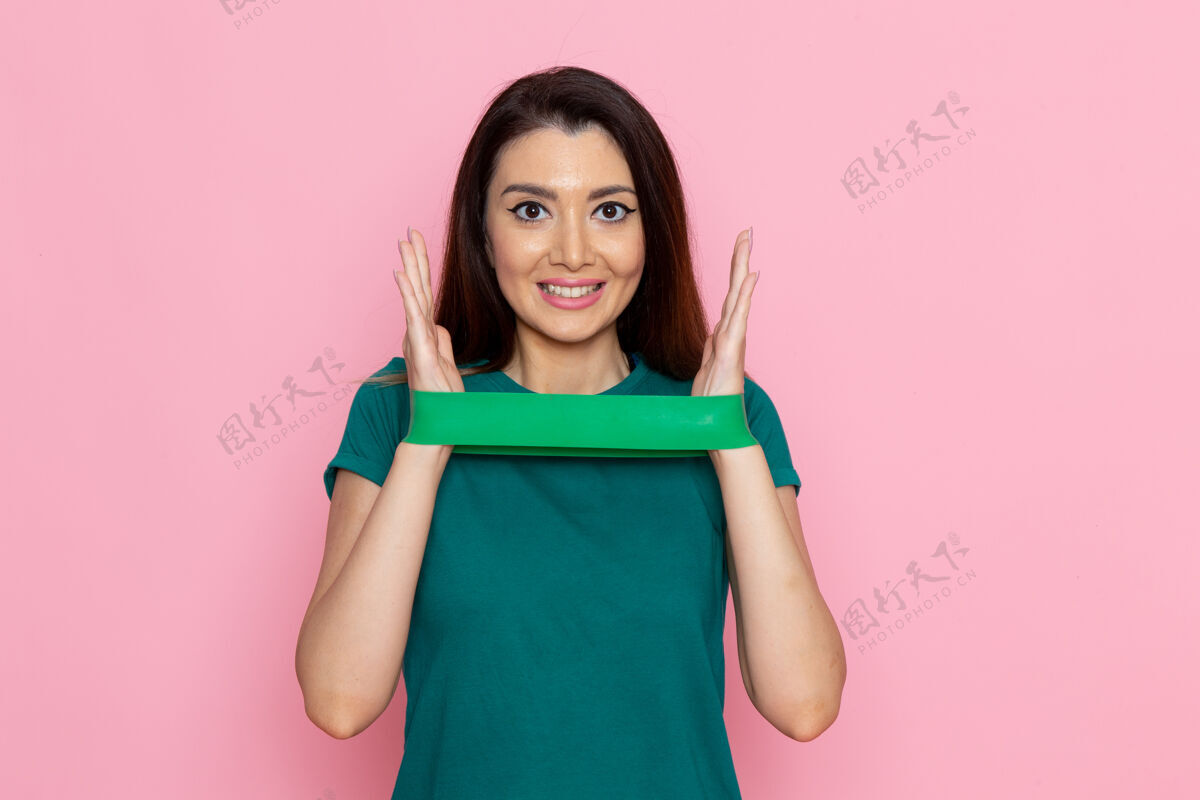 运动正面图年轻女性手持绿色绷带 微笑着站在浅粉色的墙上运动锻炼运动员美女运动员锻炼女性