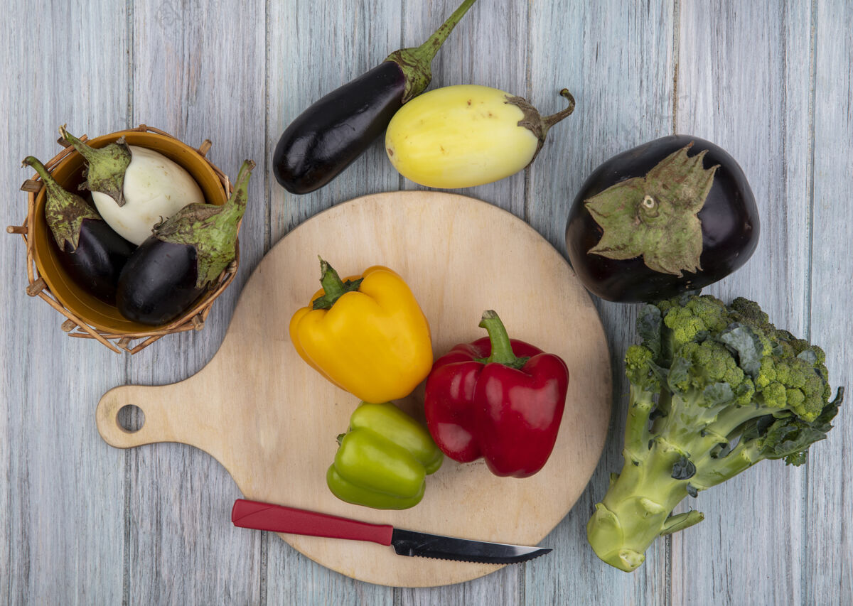 食物切菜板上有刀的辣椒和木制背景上有西兰花的茄子等蔬菜的俯视图顶部切西兰花