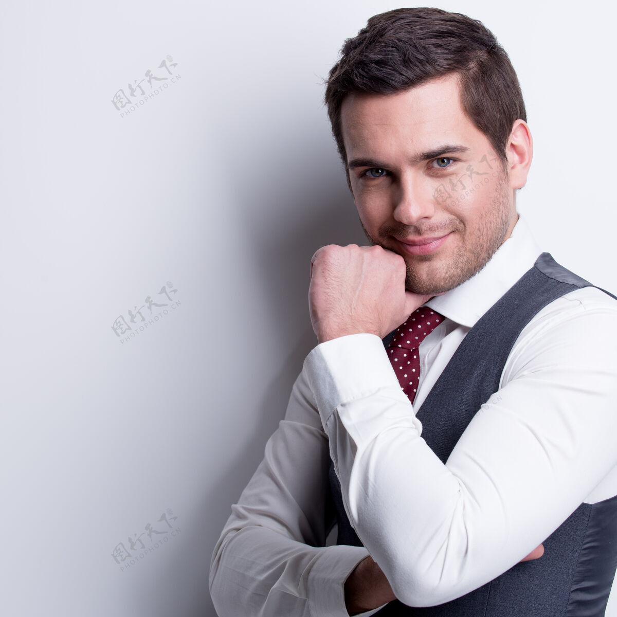 商务男士身着灰色西装 手贴脸的年轻商人的肖像在墙上摆姿势帅气快乐年轻