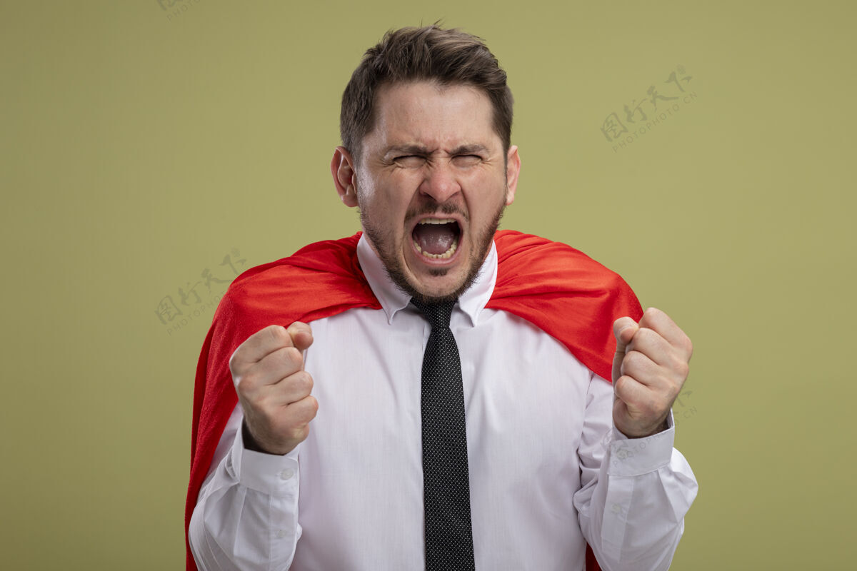 超级英雄疯狂愤怒的超级英雄商人 穿着红色斗篷 握紧拳头 表情凶猛 站在绿色的墙上狂吼超级拳头斗篷