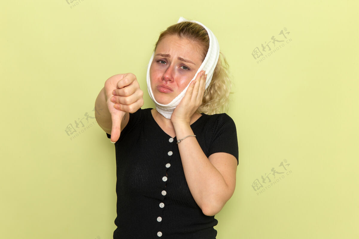 感情正面图年轻女子头上围着白毛巾 感觉很不舒服 病痛的绿色墙上牙疼生病的女健康女孩年轻毛巾头