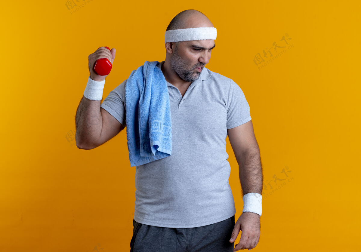 哑铃成熟的运动型男人戴着头巾 站在橘色的墙上 哑铃看起来很疲惫 精疲力尽看运动市民