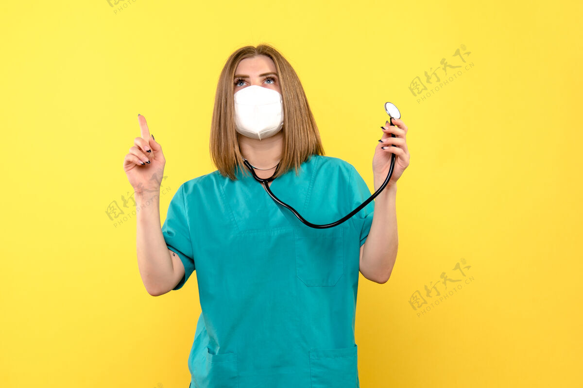 专业黄色墙上戴着无菌口罩的女医生的正视图正面设备微笑