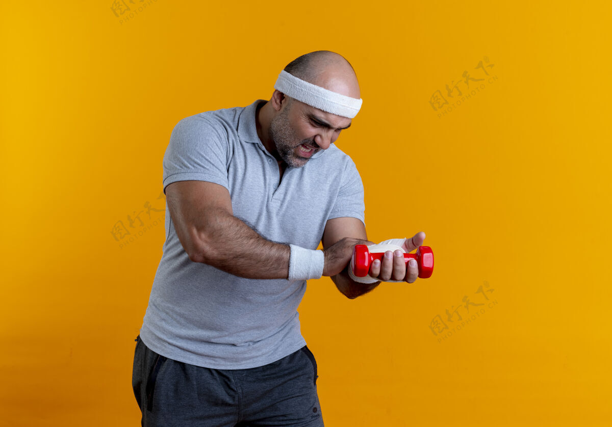 人戴着头巾的成熟的运动型男人站在橘色的墙上 摸着他缠着绷带的手 看起来很不舒服成熟人头带