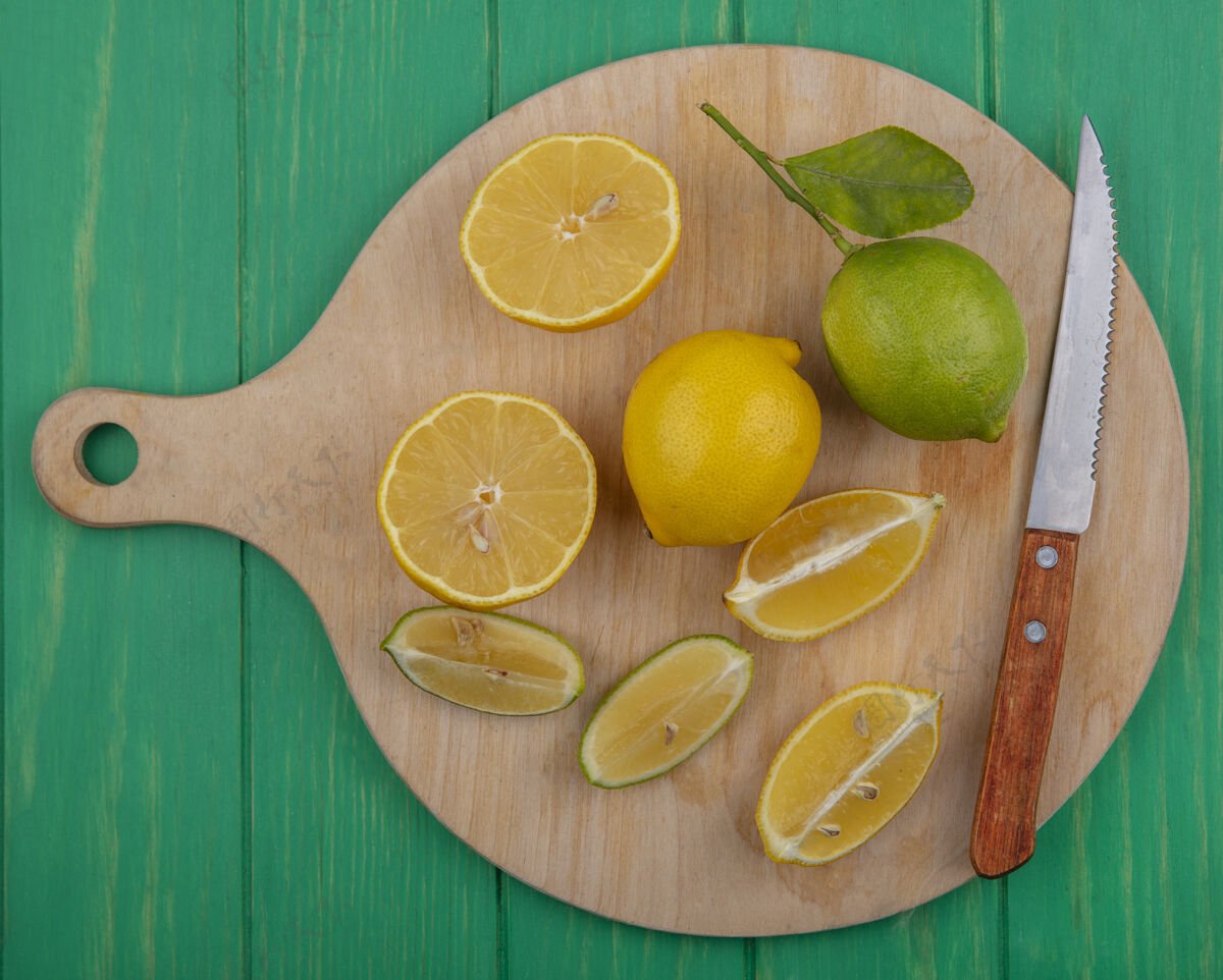 水果顶视图柠檬片和一把刀在一个绿色背景的砧板上绿色柠檬刀