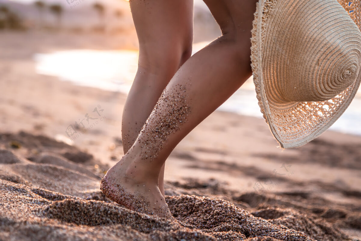 夏天身体的一部分日落时分一个戴着帽子站在海滩上的女人的脚休息帽子特写