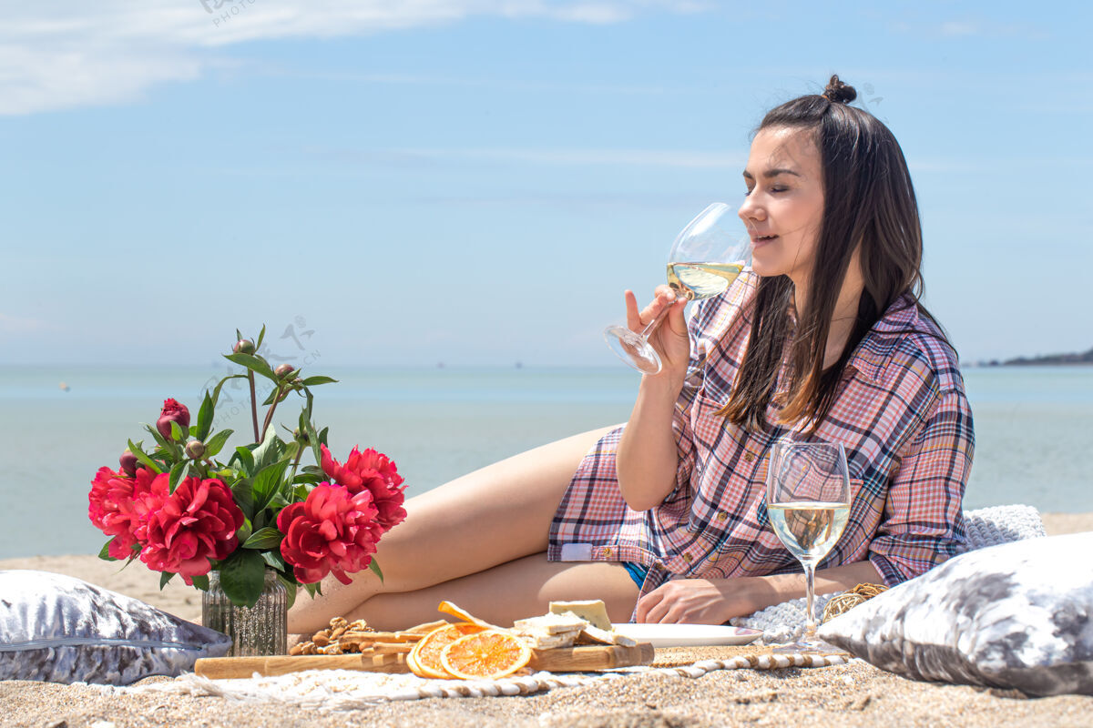 海滩一个浪漫的野餐在沙滩沙滩上与鲜花和饮料杯暑假的概念黑发优雅享受