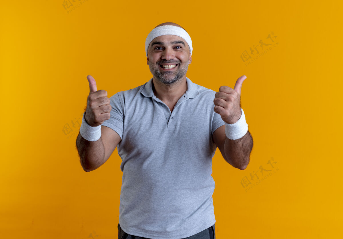 男性戴着头巾的成熟运动型男人站在橙色的墙上 面带微笑 竖起大拇指站在前面运动运动装脸