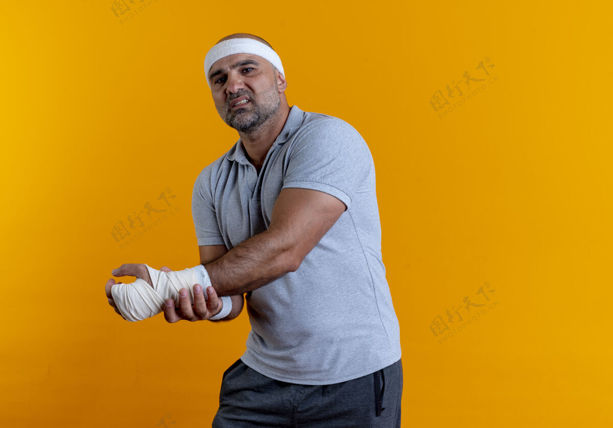 运动戴着头巾的成熟的运动型男人站在橘色的墙上摸着他的手 看起来很不舒服男手人