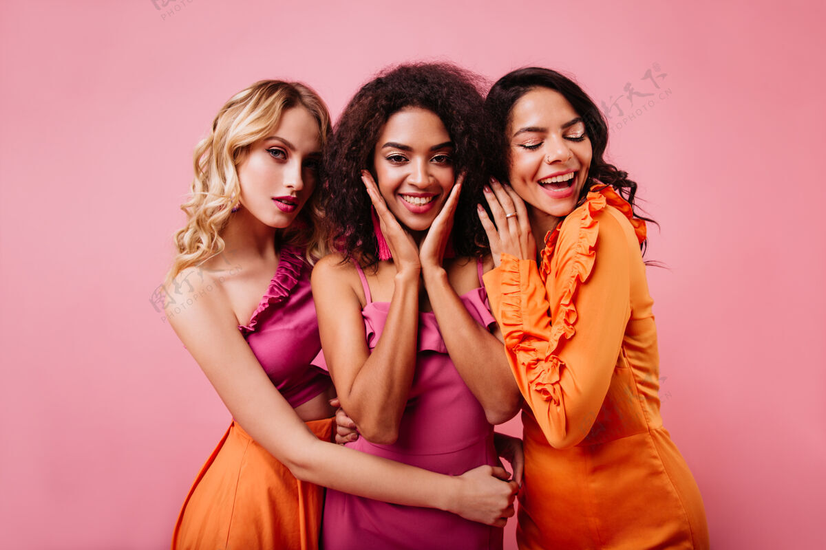 友谊三个可爱的女人在粉红色的墙上合影时尚卷发朋友