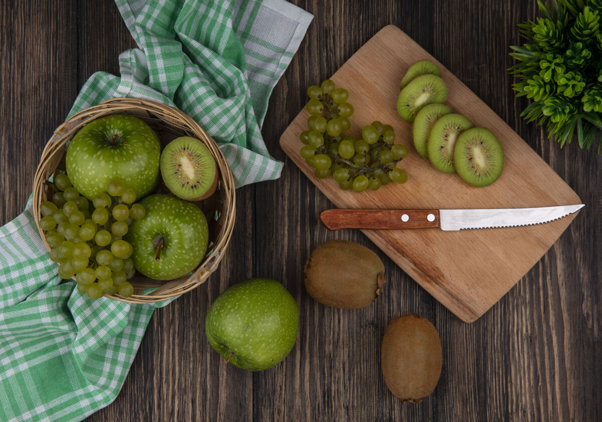 葡萄顶视图绿色葡萄与猕猴桃片和一把刀在板上和绿色的苹果在一个绿色格子毛巾篮子在木制背景上板苹果木头