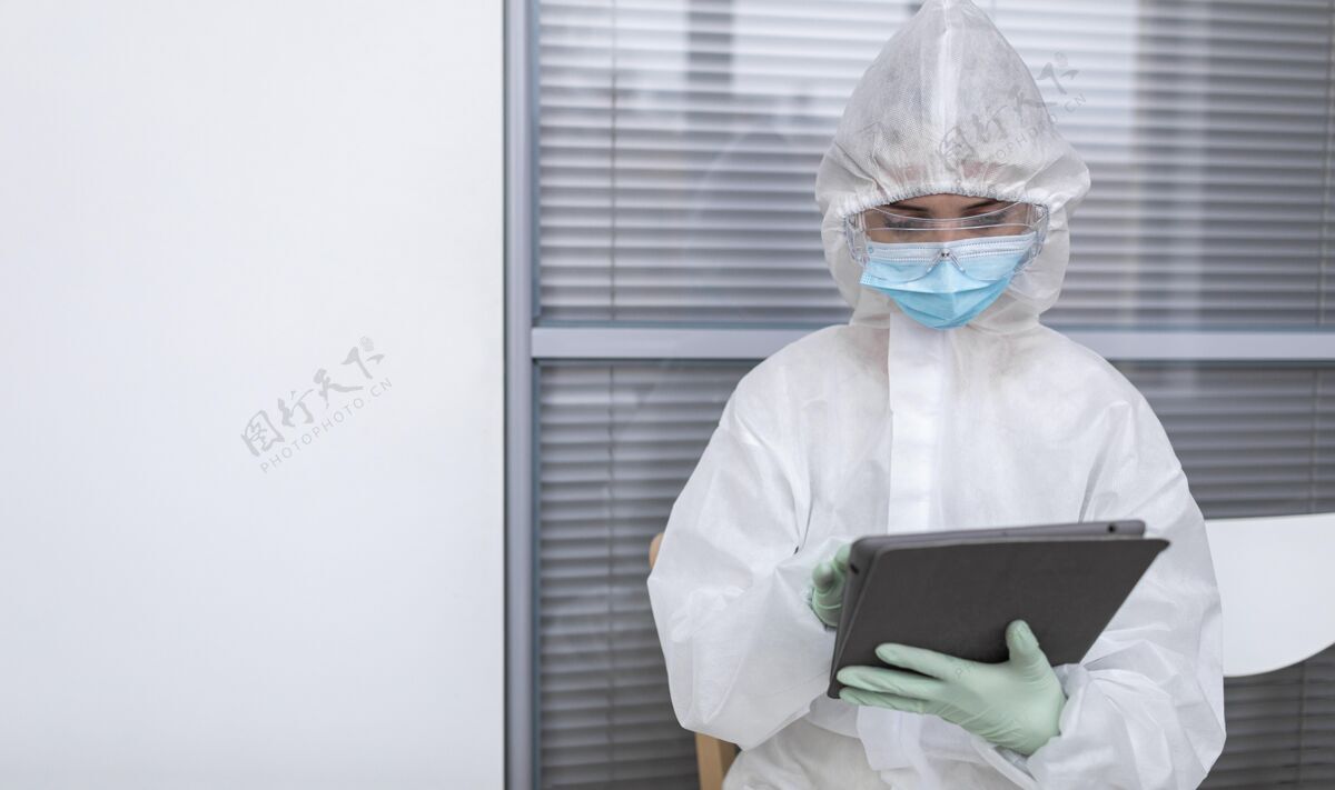 冠状病毒穿防护服的人看着平板电脑防护服预防生物危害