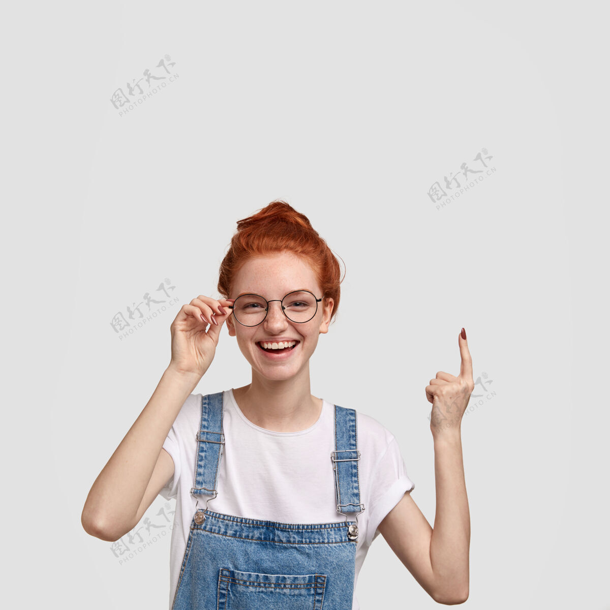 积极快乐微笑的姜发雀斑女孩垂直镜头 食指向上指 为你的广告展示自由空间 手放在眼镜边 表达快乐青少年指向广告