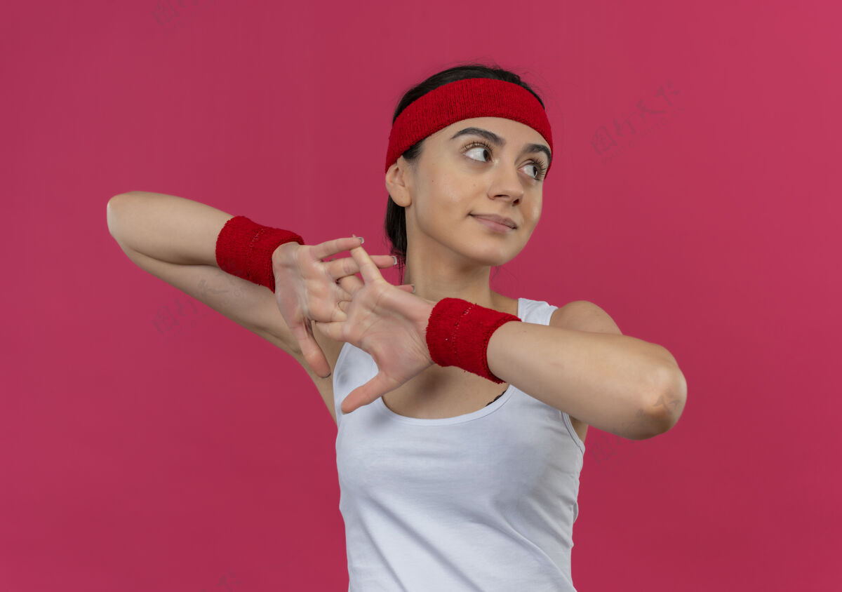 运动身穿运动服的年轻健身女士戴着头巾站在粉红色的墙上热身健身运动员健康