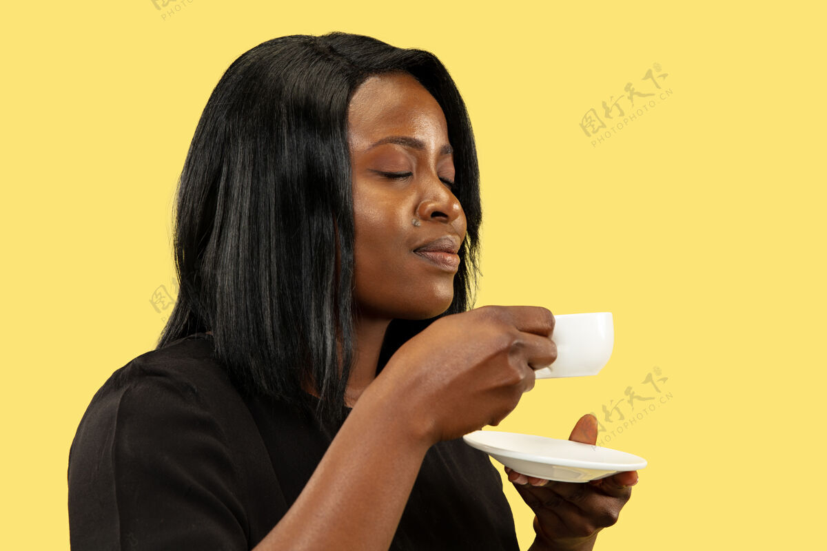 黑发年轻的非洲裔美国女性 隔离在黄色的工作室背景下 面部表情美丽的女性半身像人类情感的概念 面部表情喝咖啡的享受欢呼经理人