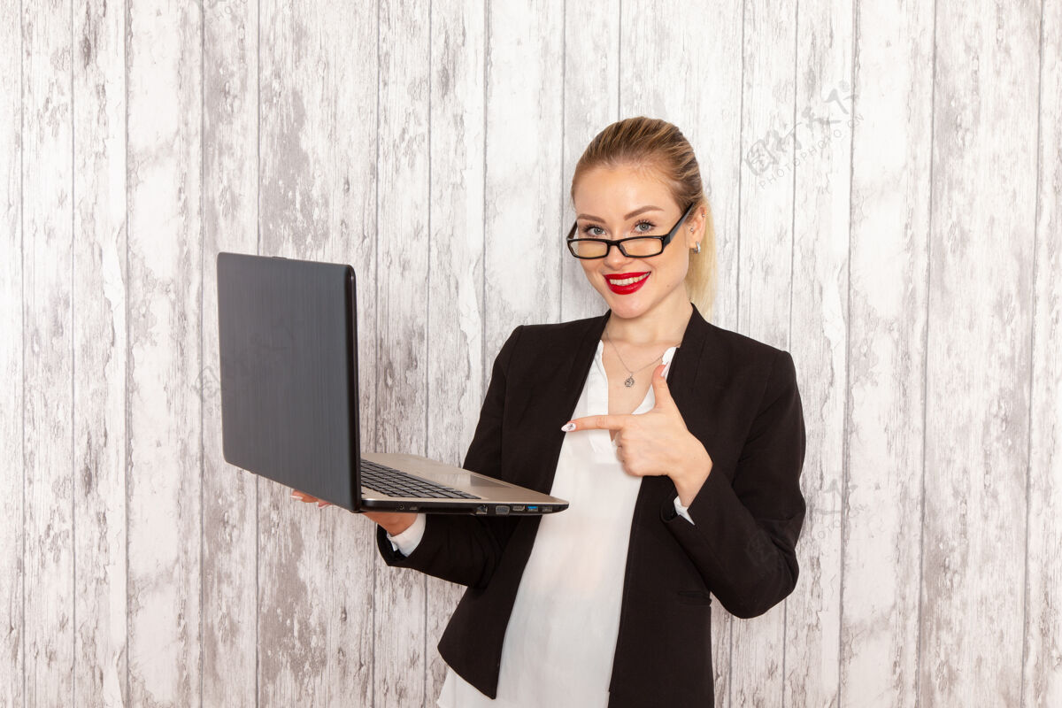 衣服正面图：穿着黑色夹克的年轻女商人在浅白的办公桌上使用笔记本电脑前台商务男士办公桌