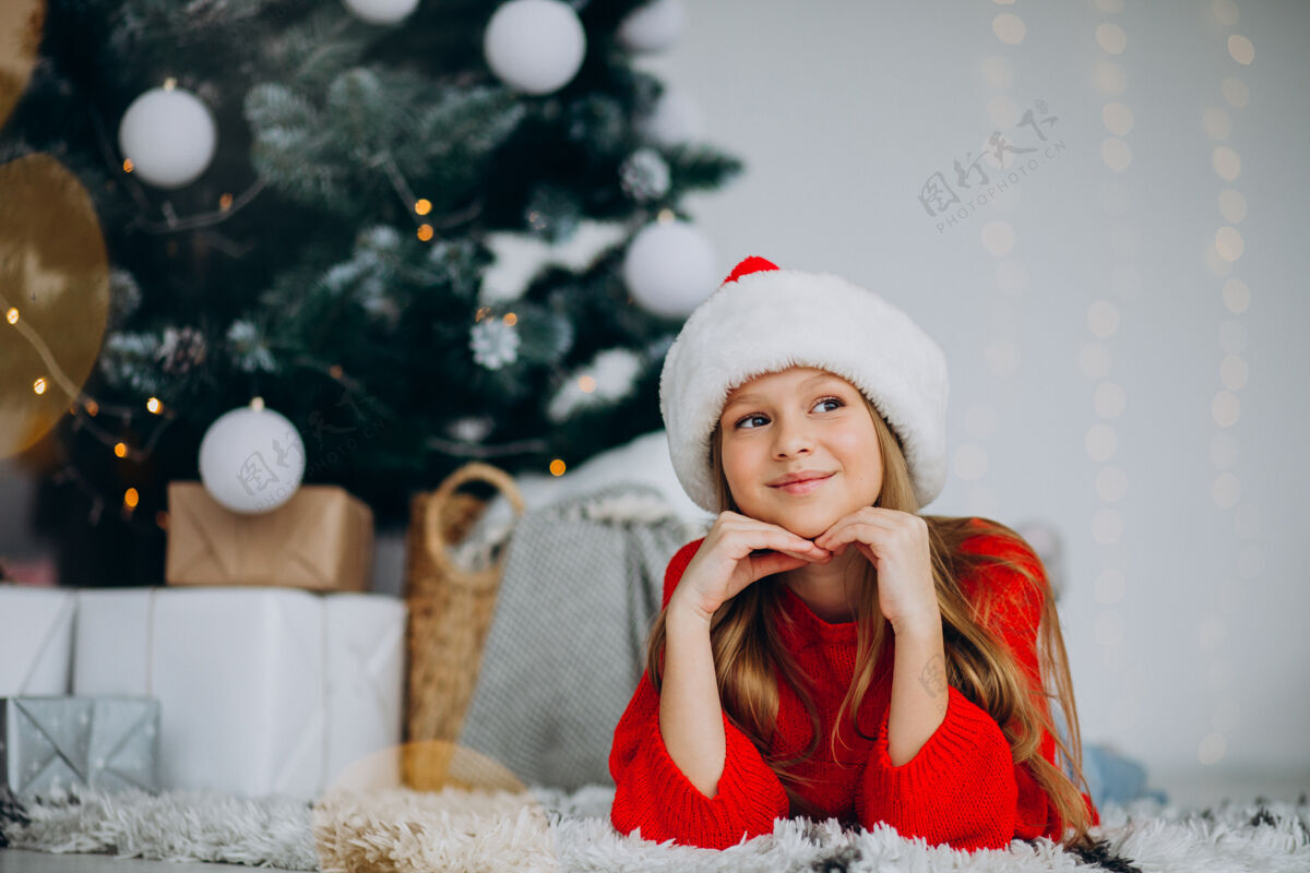 礼物圣诞树下戴圣诞帽的漂亮女孩庆祝平安夜圣诞老人