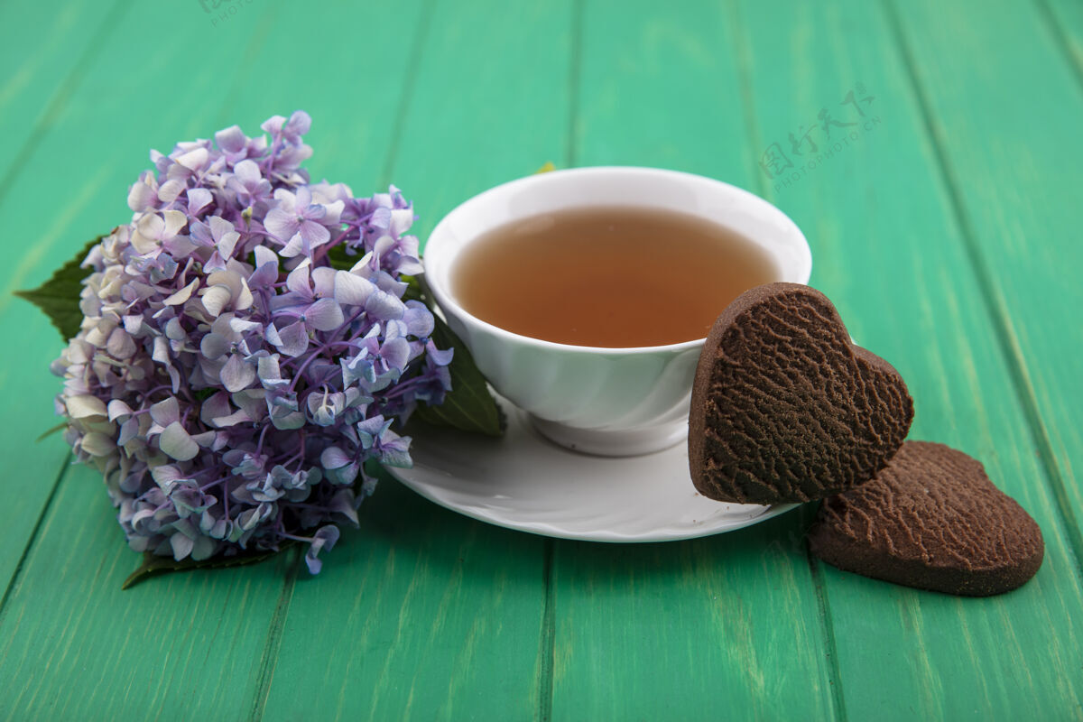 绿色茶杯和心形饼干的侧视图 绿色背景上有花朵桌子杯子饮料