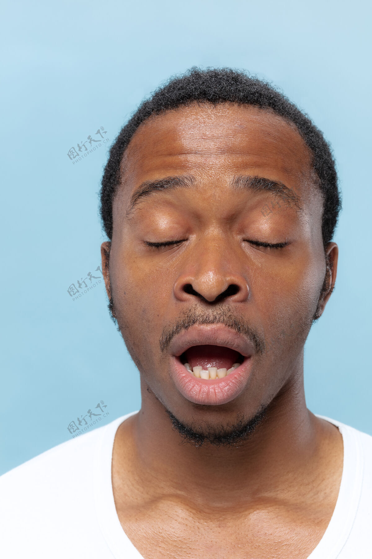 就业在蓝色背景上的穿着白衬衫的非洲裔美国年轻人的特写肖像人类的情感 面部表情 广告 销售观念打喷嚏前几秒钟表情专业肖像
