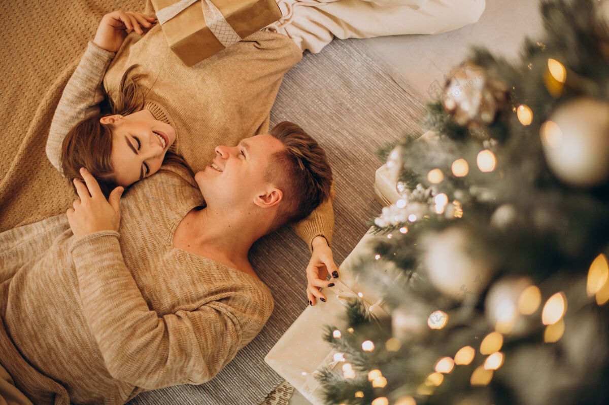 年轻一对年轻夫妇在圣诞树旁互相制作礼物情人圣诞礼物现代