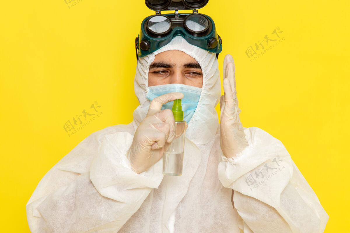 持有正面图穿着特殊防护服的男性科学工作者拿着喷雾剂在黄色表面上使用它前面使用特殊