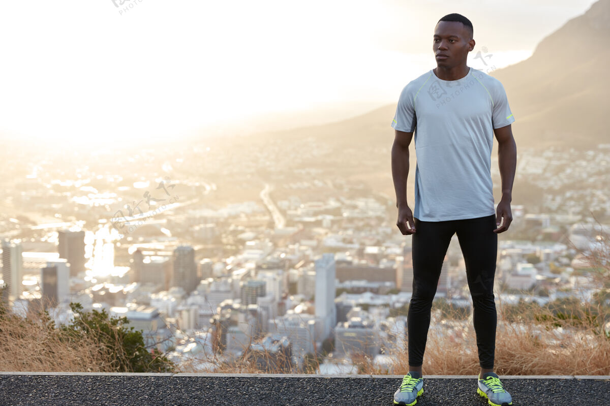 教练体格健康体贴的运动型男士 站在山上与城市景观相对 穿着休闲服 左侧为您的广告内容腾出空间人 动力和能量的概念自由空间城市沥青