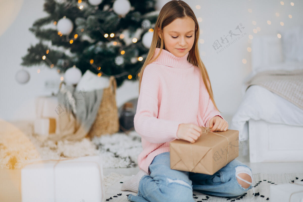 毛衣可爱的女孩拿着圣诞礼物在圣诞树旁看光明灯