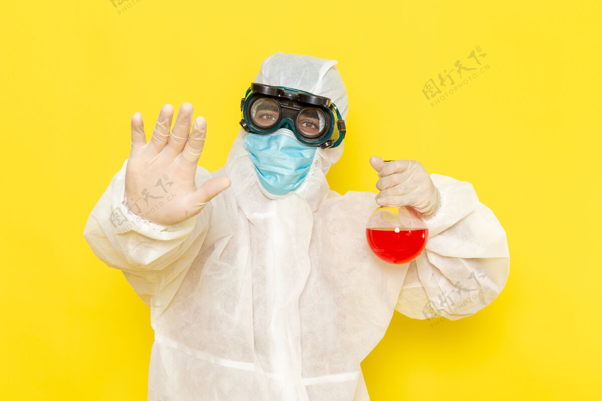 科学正面图穿着特殊防护服的男科学工作者在黄色的桌子上拿着装有红色溶液的烧瓶保温瓶正面特殊
