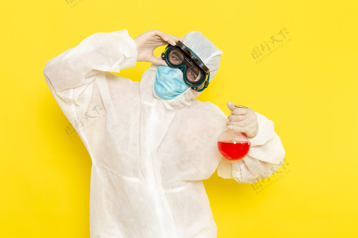 化学正面图穿着特殊防护服的男科学工作者在黄色的桌子上拿着装有红色溶液的烧瓶正面实验服服装