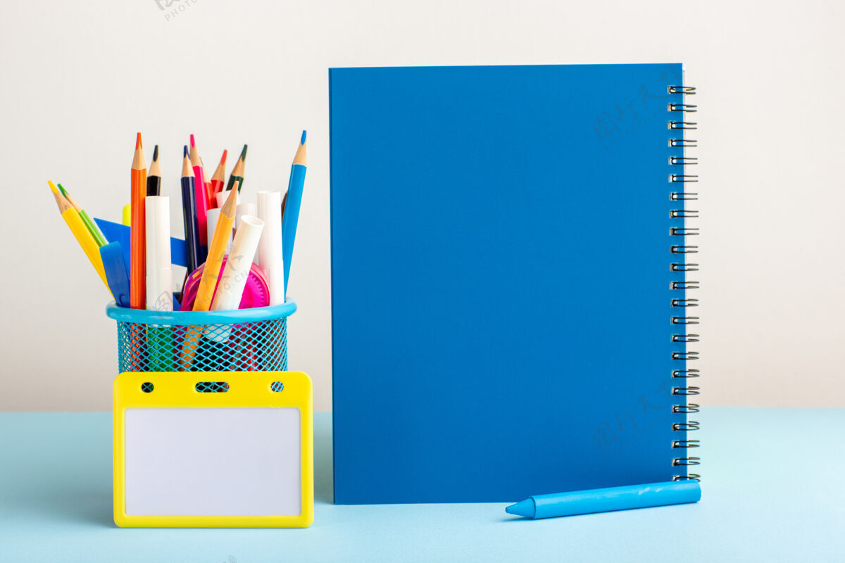 笔记本电脑正面图蓝色书桌上有不同颜色的铅笔和蓝色的抄写本电脑屏幕学校