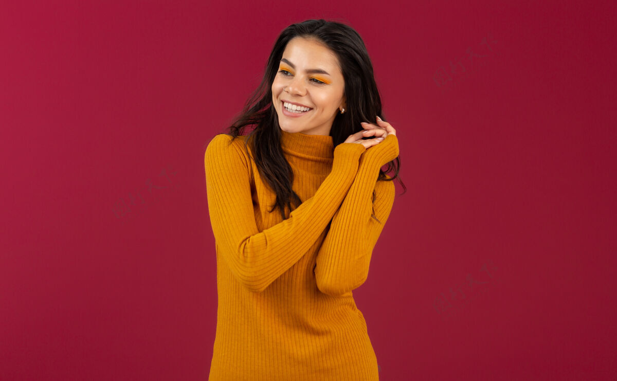 模特美丽的微笑 时尚的深色皮肤 穿着黄色秋冬时装毛衣的西班牙女人的画像 在红墙上摆出孤立的姿势颜色优雅魅力