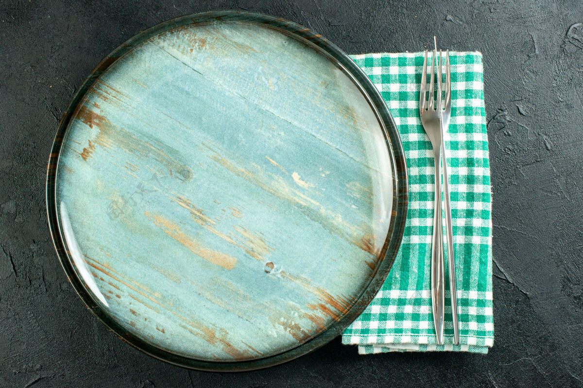 陶器顶视图圆形拼盘餐刀和餐叉在绿色和白色格子餐巾在黑色表面培养皿视图盘子