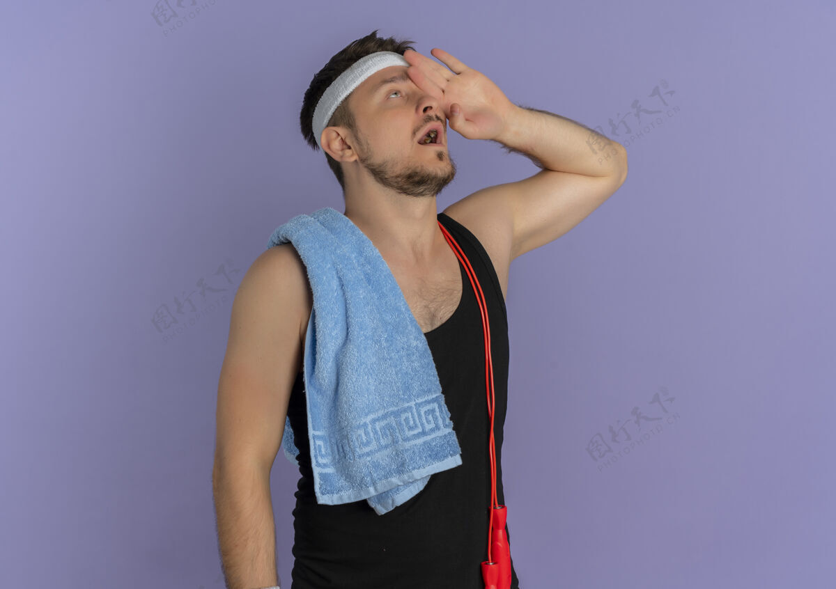 运动戴着头巾 肩上扛着毛巾 手举着头 站在紫色墙壁上的年轻健身男子男头带教练