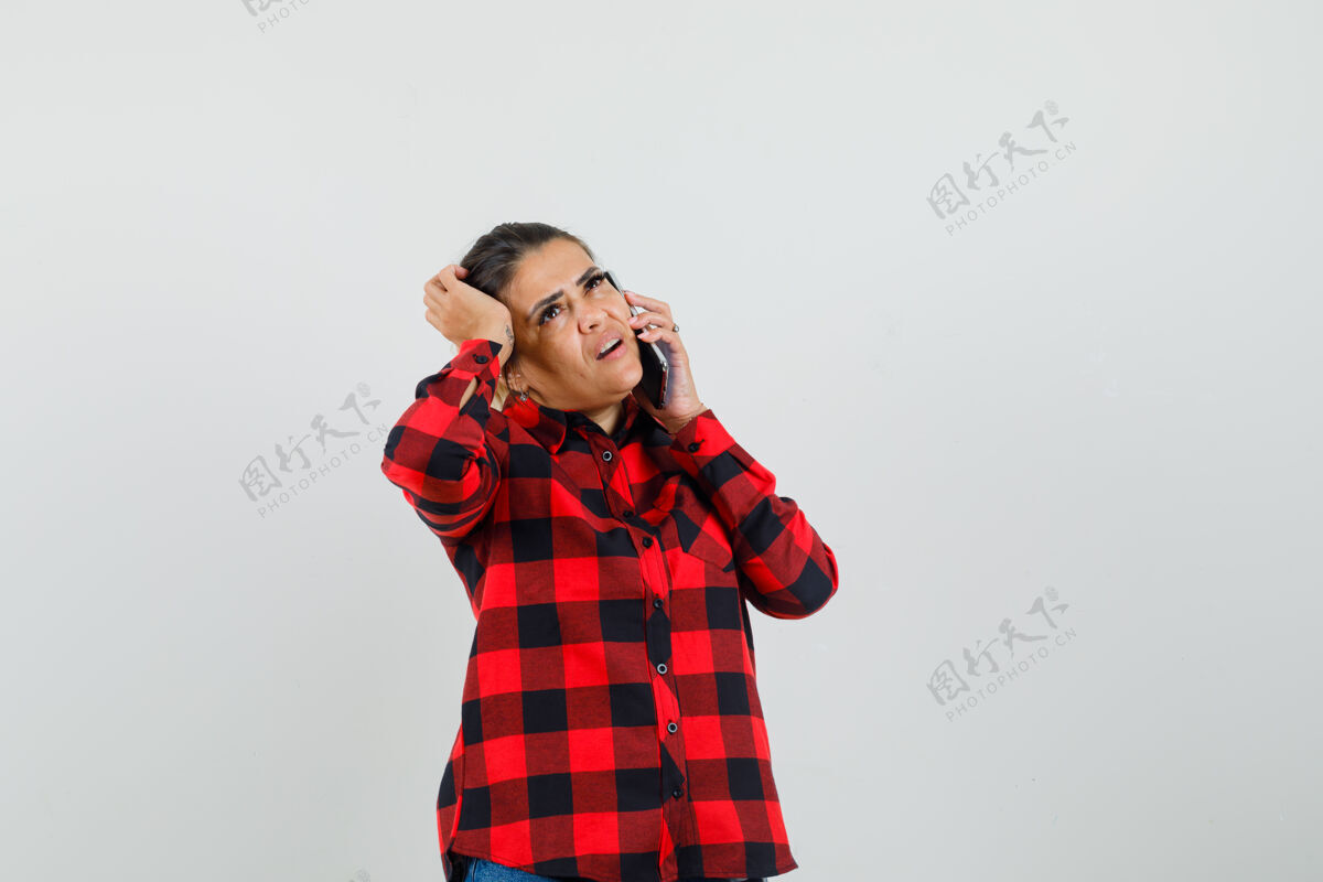 女孩年轻女子在讲手机 在格子衬衫挠头 看起来沉思 前视图积极时尚时尚