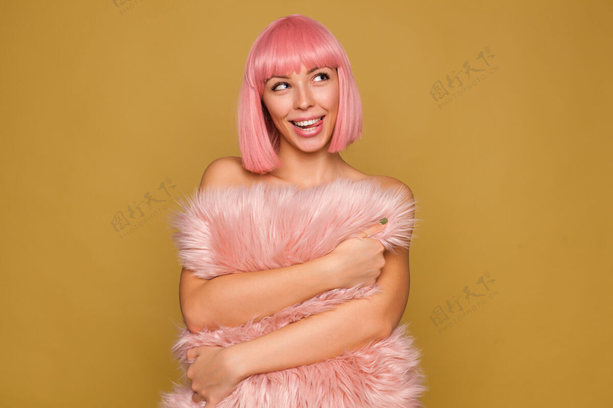 枕头梦幻般的年轻可爱开朗的女性 粉色的bob发型伸出舌头 一边开心地看着一边 一边抱着粉色毛茸茸的枕头 一边在芥末墙上摆姿势特写动漫姿势