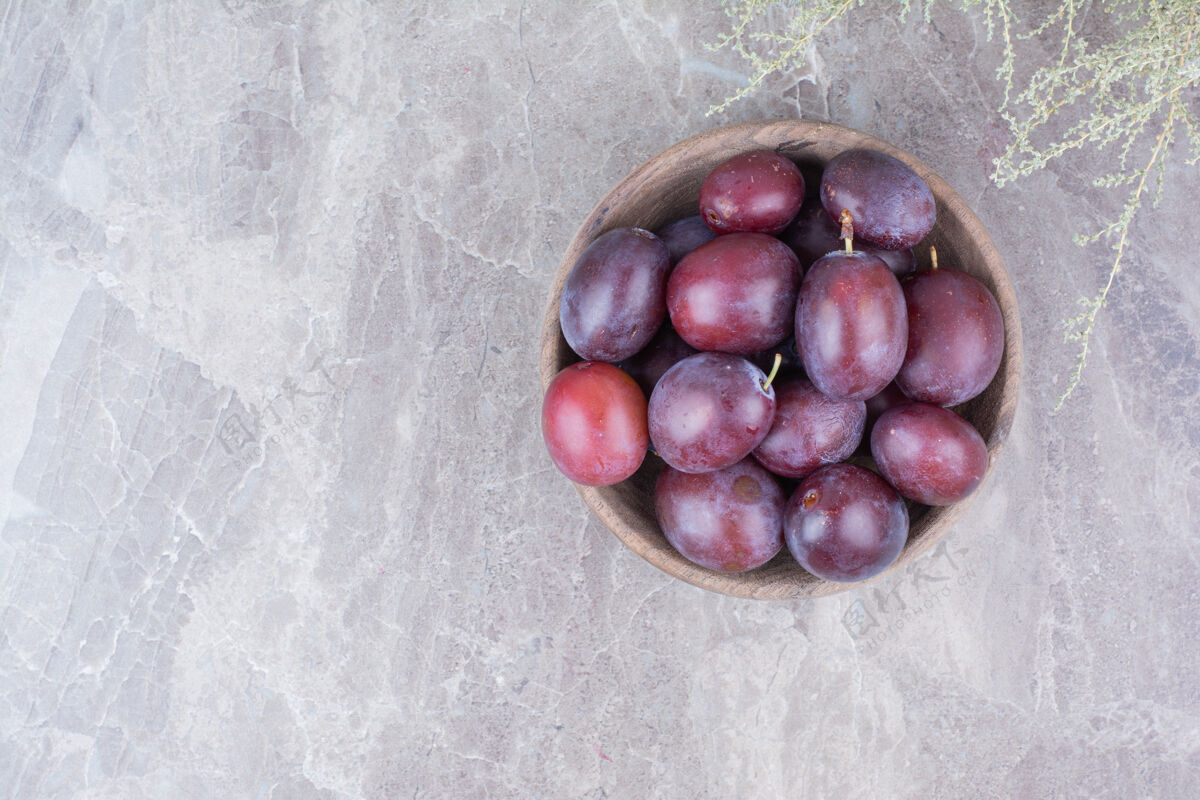 健康紫色李子放在石头背景的木碗里李子新鲜美味