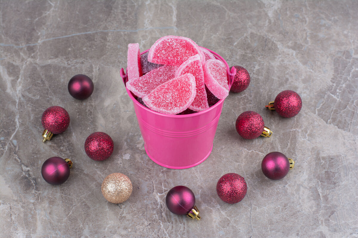 糖果一个粉红色的桶里装满了甜甜的果酱 大理石背景上有红色的圣诞球美味美味果冻