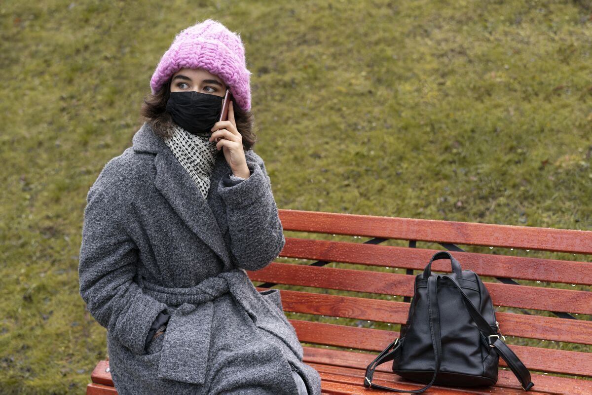 人类城里戴着医用口罩的女人在长凳上打电话预防措施病毒新常态