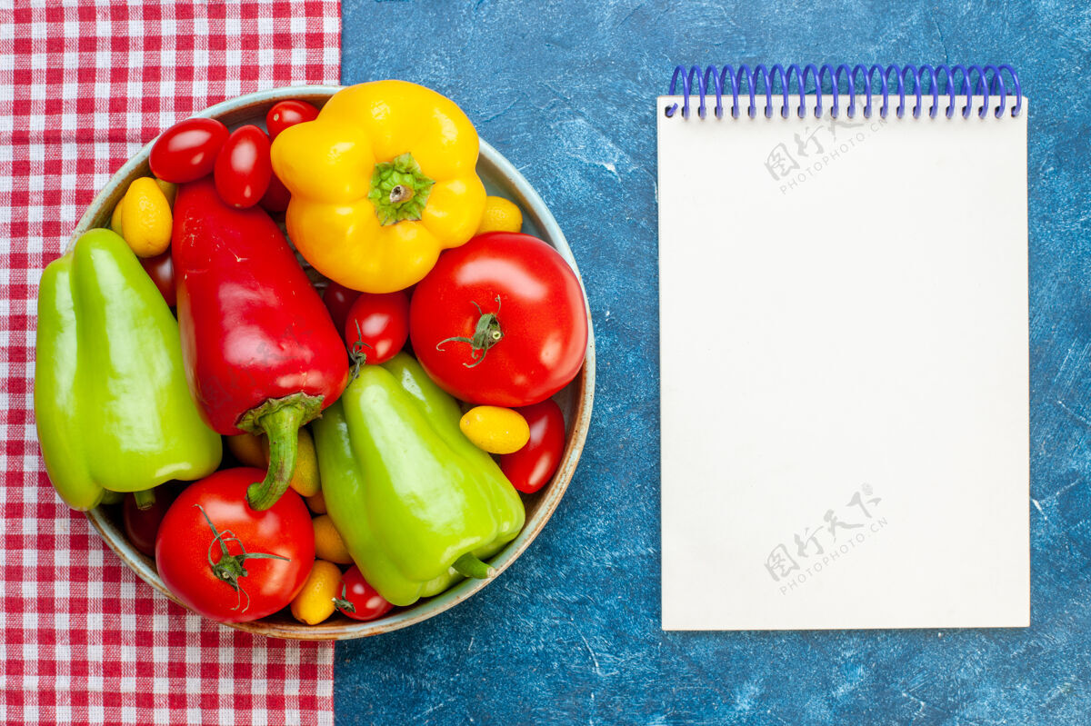 笔记本顶视图新鲜蔬菜樱桃西红柿不同颜色甜椒西红柿孜然在盘子上红色和白色格子桌布笔记本在蓝色的桌子上桌面颜色铃铛