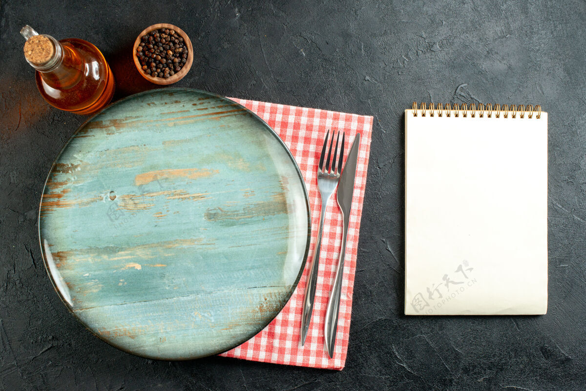 餐巾俯视图圆形拼盘餐刀和叉子在红白格子餐巾笔记本上黑桌子上叉子顶部笔记本