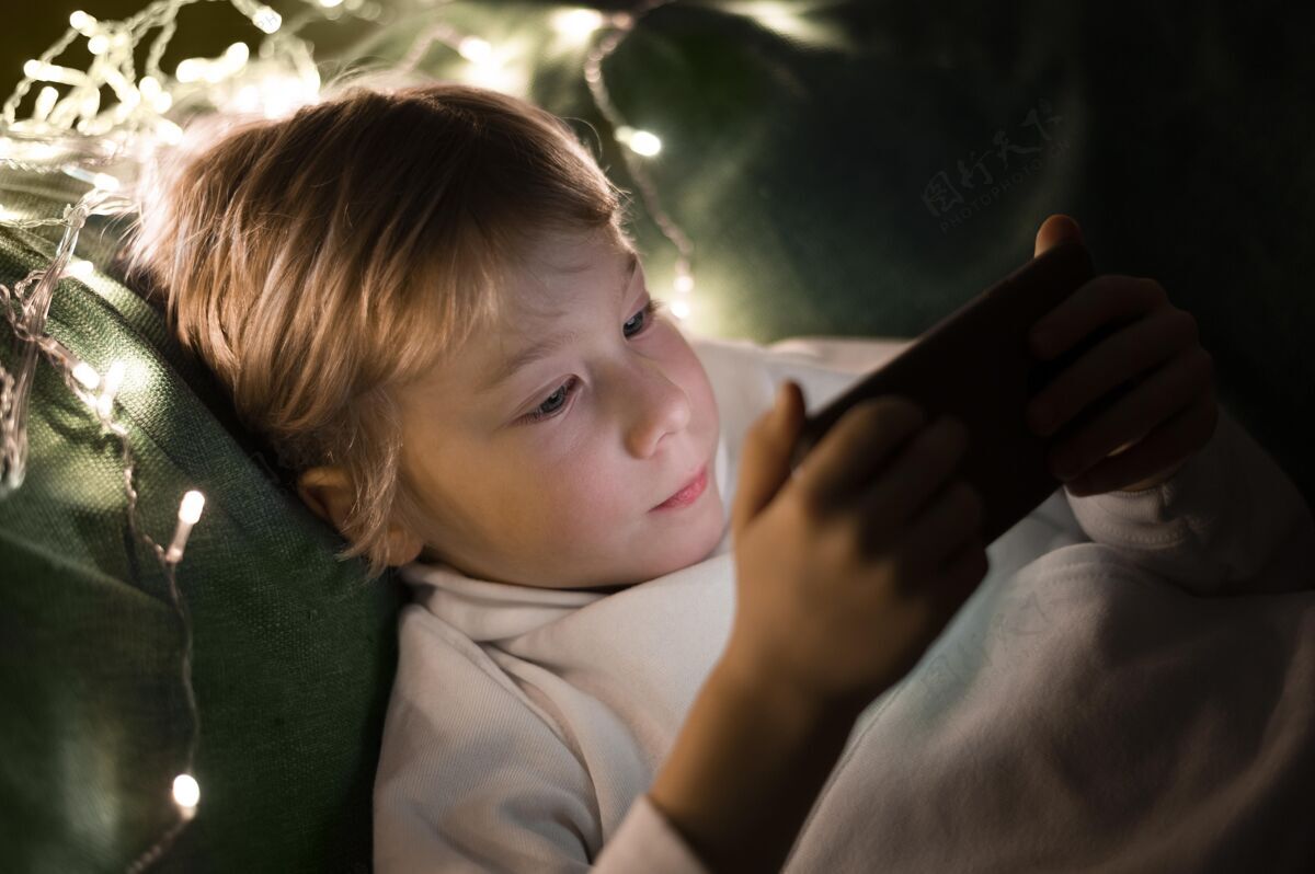 设备小男孩晚上在床上用智能手机消遣青年男孩