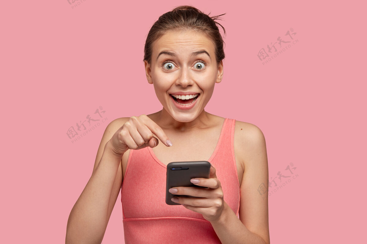 女性正惊讶的年轻女性指着手机屏幕手机照片指向